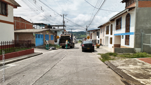 garbage collectors loading waste into a sanitation truck on a quiet town street in colombia