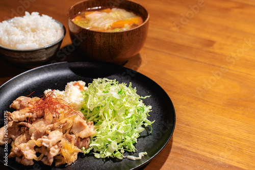 Photos 木目調のテーブルに配置された豚の生姜焼き定食の俯瞰気味の写真。バナーやメニュー用