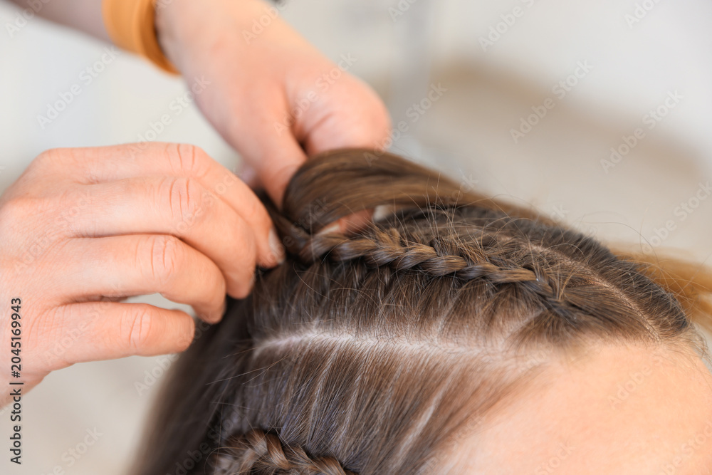 Fototapeta premium Hairstylist braiding teenage girl's hair indoors, closeup
