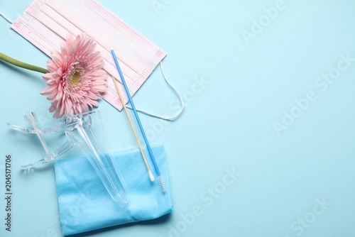 Sterile gynecological examination kit  medical mask and gerbera flower on light blue background  flat lay. Space for text