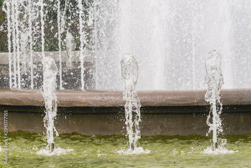 Water fountain spraying upward in stone basin. Jets of water splashing in park pool. Urban architecture, exterior city decor, fresh environment, summer background, fluid motion design.