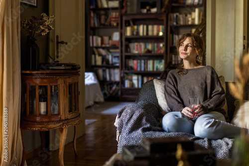 Fotografía Young woman comfortably relaxing on a patterned sofa in a warm living room, hold