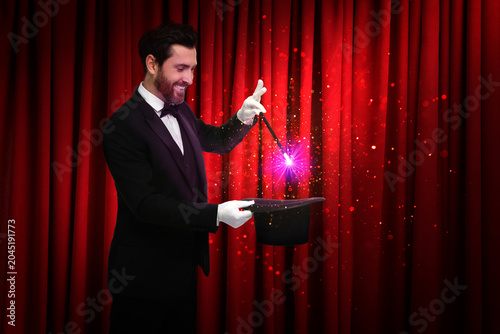 Foto Magician performing trick with top hat on stage against red curtains