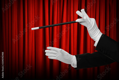 Tableau sur toile Magician performing trick with wand on stage against red curtains, closeup