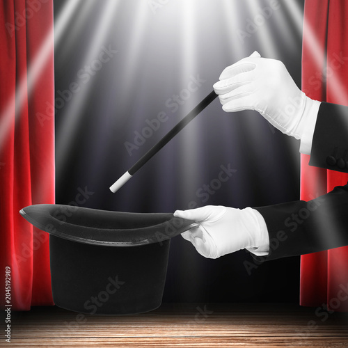 Foto Magician performing trick with wand and top hat on stage against red curtains, c