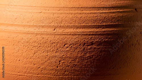 Close-up of a textured, orange terracotta pot with horizontal lines and rough surface details in warm lighting conditions