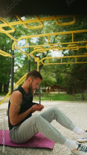 A determined young man pauses to wipe sweat from his face during an outdoor calisthenics workout. He is taking a brief break from his intense fitness routine at the park gym