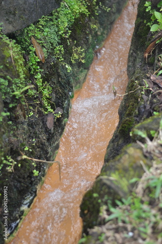 A river with brown water flowing through a rocky area. The water is murky and has a brownish tint