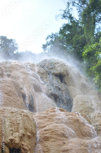 A waterfall is spraying water over a rocky cliff. The water is white and misty, creating a serene and peaceful atmosphere. The scene is a beautiful example of nature's power and beauty