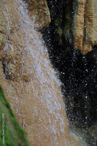 A waterfall with a brownish color and white water. The water is falling from a cliff and creating a misty atmosphere