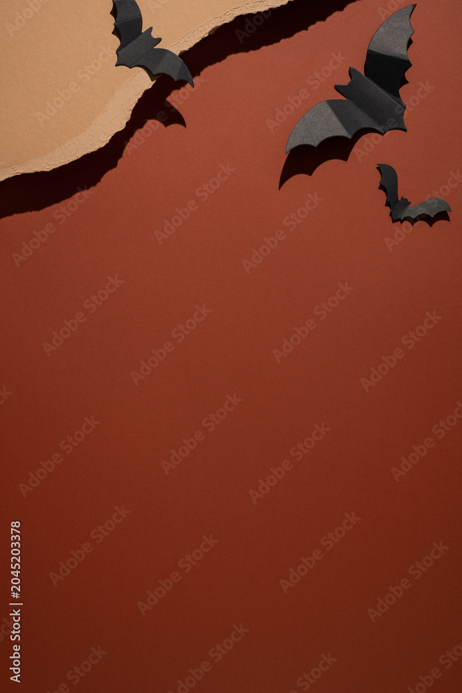 Fototapeta premium Happy Halloween paper bat decorations on torn brown and orange background with vertical strong shadows