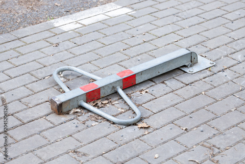 Metal parking barrier with red markings lying on a paved surface, surrounded by fallen leaves and gravel, indicating a designated parking area