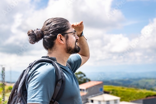 Man with backpack shielding eyes looking at sunny mountain view