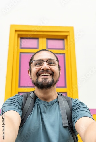 Happy man with backpack taking vertical selfie by colorful door