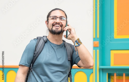 Smiling man with backpack talking on phone by colorful wall