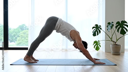 Man practicing yoga downward dog pose in bright home
