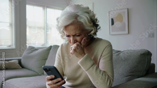 Mature woman looking at smartphone with concerned facial expression while sitting on sofa