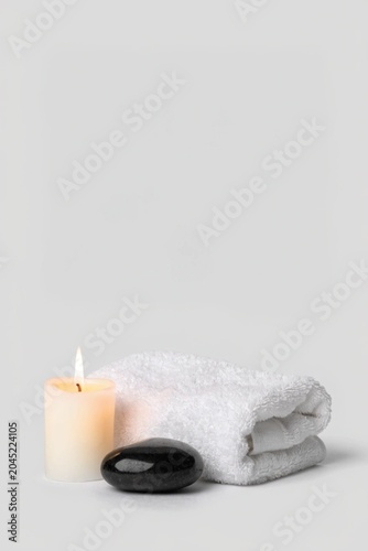 Spa setup with white towel, candle and black stone at the light grey background. Copy space