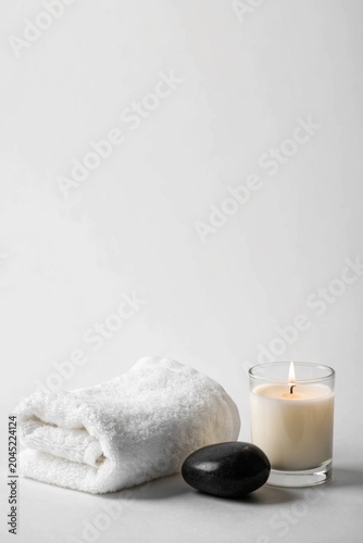 Spa setup with white towel, candle and black stone at the light grey background. Copy space