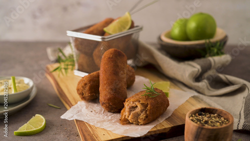 Foto Crispy golden-brown croquettes are arranged on a rustic wooden board with one broken open to reveal the savory meat filling