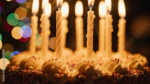 Lit white candles on birthday cake with colorful bokeh background