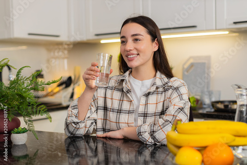 Young woman drinks chilled filtered water from glass in kitchen, easing thirst and keeping hydrated. Simple hydration habit supports healthy lifestyle, and this girl enjoys a refreshing break at home.