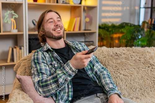 Photography Young man on home sofa switches channels with remote control finds funny show and laughs with delight