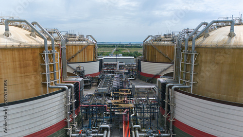 Aerial view of Grain LNG terminal featuring massive storage tanks and intricate industrial piping under a cloudy sky Wallend, England, United Kingdom.