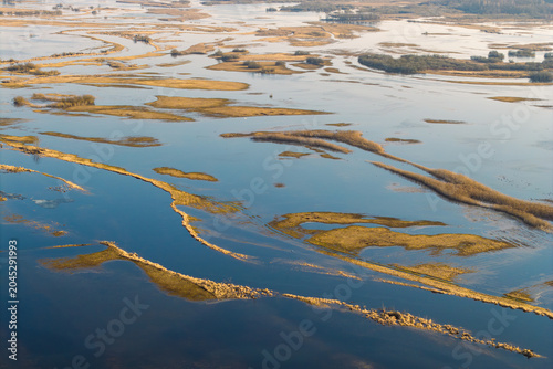 Aerial view of the Biebrza River valley with flooded meadows, winding water channels, and dry reeds under soft light in Podlaskie Voivodeship, Poland.