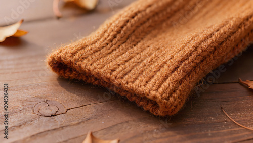 Cozy Autumn Knitted Fabric Texture with Fallen Leaves on Wooden Surface
