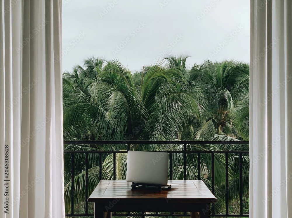 Obraz premium Laptop on balcony table with tropical palm tree view, a computer setup