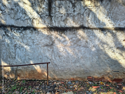 Concrete wall texture with rough surface, tree shadows, and dirty ground detail