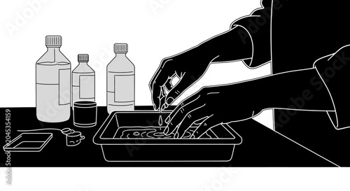 Tableau sur toile A person developing photographic film in a darkroom tray with chemical bottles