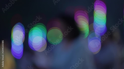 Close up colorful illumination bokeh background with blurred silhouettes of people walking past neon light decorations at night temple festival fair.