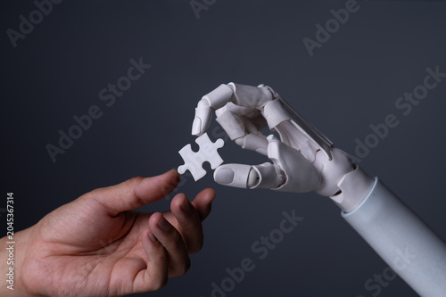 Robot hand passing a jigsaw puzzle piece to a human hand.