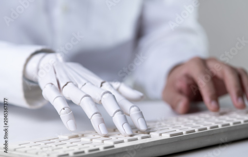 Robot and human hands typing on computer keyboard together.