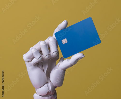 Robotic hand holding blank blue credit card on yellow background.