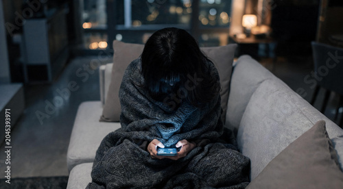 Technology addiction and sleep disorder concept with woman looking at bright phone screen wrapped in cozy blanket