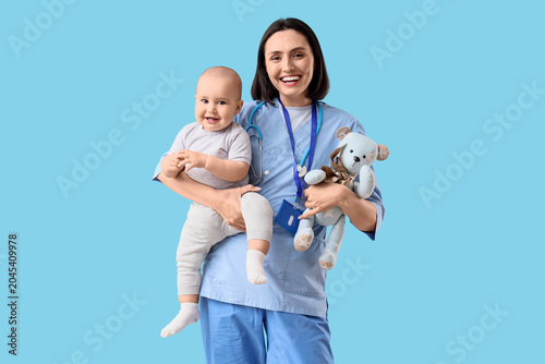 Cuadro en lienzo Young female pediatrician with toy and cute little baby on blue background