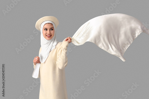 Stylish Muslim woman in white clothes on grey background