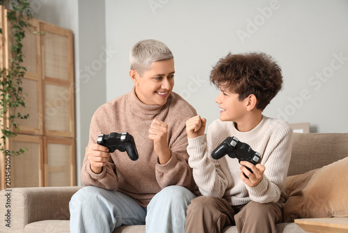 Mother and her teenage son in warm sweaters playing video game on sofa at home