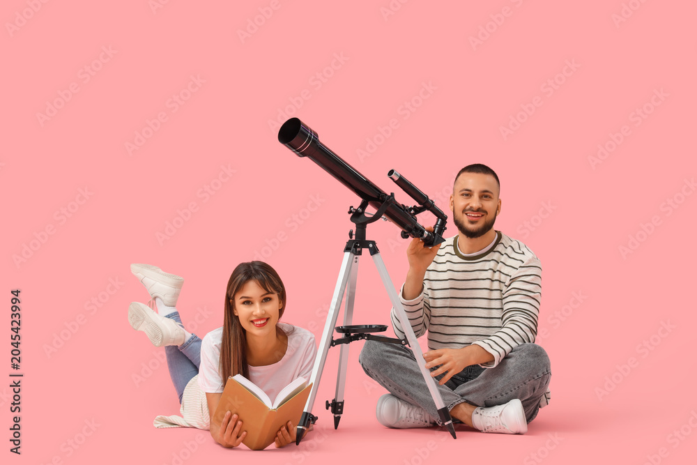 Obraz premium Young couple with telescope and book on pink background