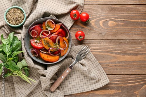 Bowl of fresh tomato salad with red onion and basil leaves on wooden background