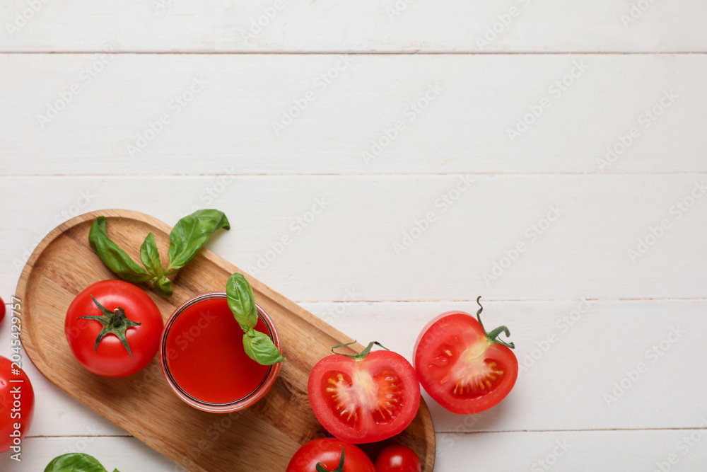 Fototapeta premium Glass of fresh tomato juice with basil and vegetables on white wooden background