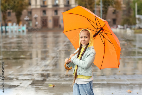 Cute little girl with umbrella on rainy day outdoors