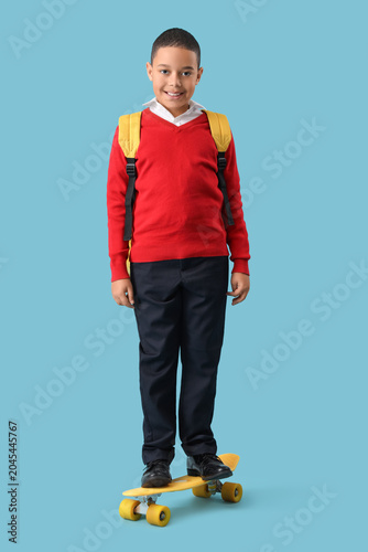 Happy little African-American schoolboy with backpack and skateboard on blue ...
