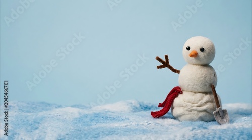 Felted snowman waving with a miniature shovel on blue background