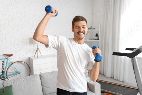 Foto Sporty young man doing exercise with dumbbells at home