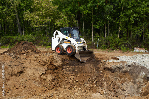 Obraz na płótnie Skid steer loader leveling soil at a construction site, working on rough terrain