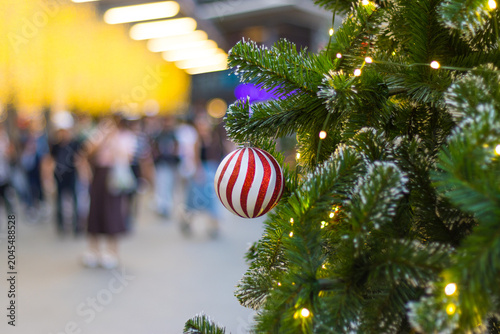 red and white striped bauble on a christmas tree. blurry people walking in the city background with bright lights